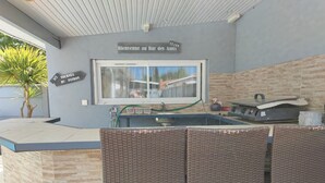 An outdoor bar area with a stone counter, wicker chairs, and a view of the house through a window. - House with a Pool: The Charm of the Pool in Gujan-Mestras (Gujan-Mestras)
