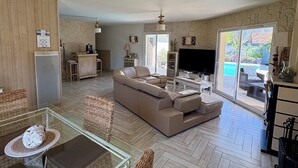 A spacious living area with a large sofa, a glass dining table, wicker chairs, a TV, and a stone wall. - House with a Pool: The Charm of the Pool in Gujan-Mestras (Gujan-Mestras)