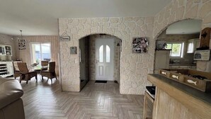 A living room with a herringbone floor, stone walls, a wooden dining set, and a kitchen area with a stone backsplash. - House with a Pool: The Charm of the Pool in Gujan-Mestras (Gujan-Mestras)
