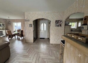 A living room with a herringbone floor, stone walls, a wooden dining set, and a kitchen area with a stone backsplash. - House with a Pool: The Charm of the Pool in Gujan-Mestras (Gujan-Mestras)