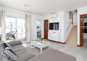 A modern living room with a sofa, a coffee table, a TV, and a staircase. - Casa Amaia - Pool Villa with Views by Villas Now (Playa Blanca)