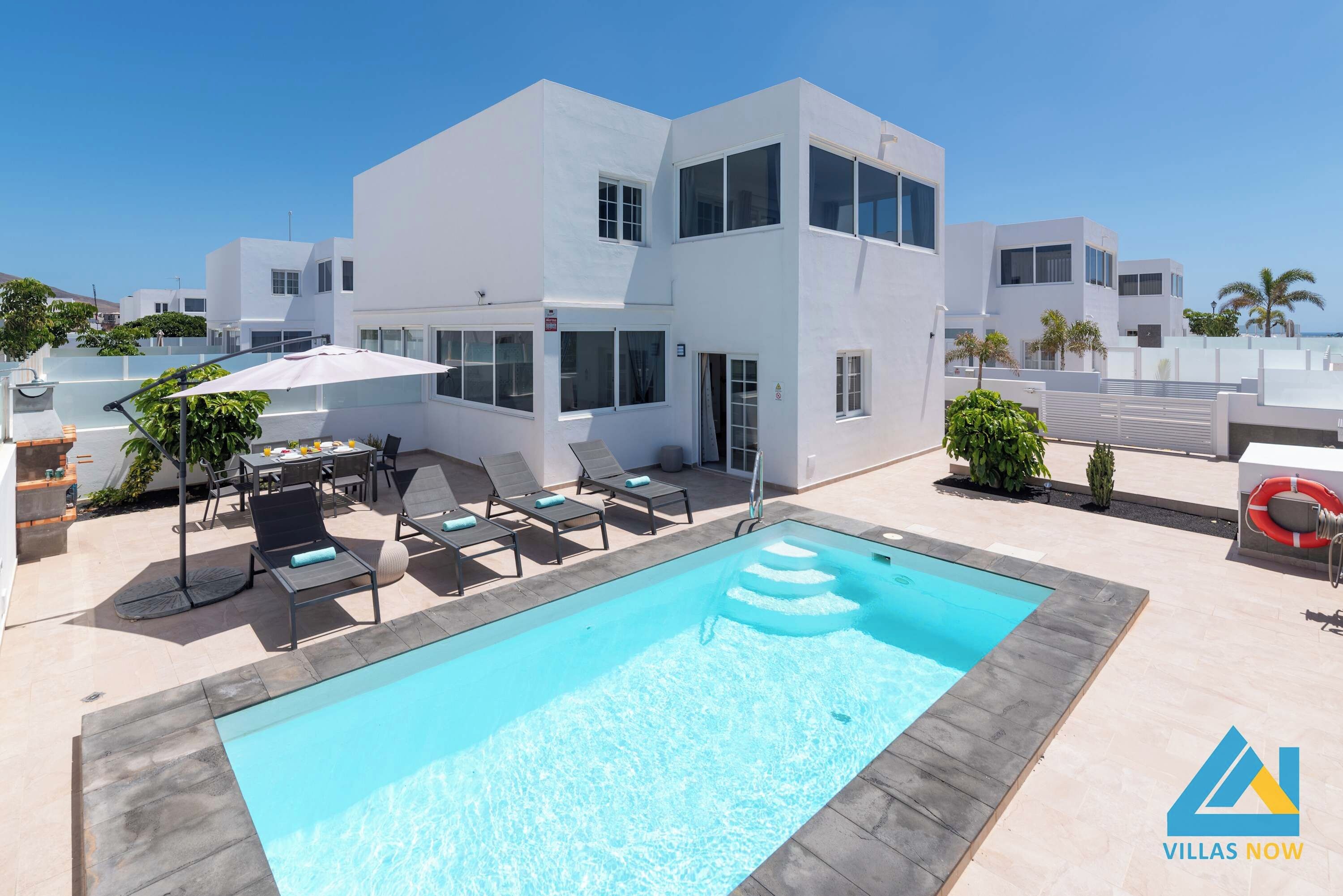 Una villa moderna con piscina, mobiliario exterior y vista despejada al mar.