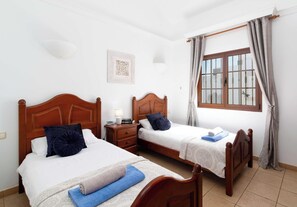 Ein Hotelzimmer mit zwei hölzernen Betten, einem Nachttisch, einem Fenster mit Vorhängen und einer Wandleuchte.