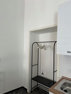 Ein kleines, kompaktes Badezimmer mit einem weißen Waschbecken, einem schwarzen Regal und einem Metalldrohgestell.