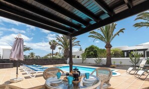 Ein Poolbereich mit Liegestühlen, einem Tisch mit Getränken und einer überdachten Terrasse.
