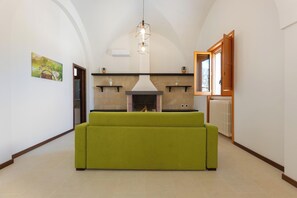 A room with a green sofa, a fireplace, a hanging light fixture, and a painting on the wall.