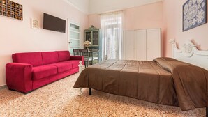 Une chambre à coucher avec un lit, un canapé rouge, une télévision, une armoire et une fenêtre avec des rideaux.