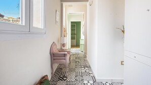 Un couloir étroit avec un revêtement de sol à motifs, une chaise, une lampe et une porte donnant sur une autre pièce.