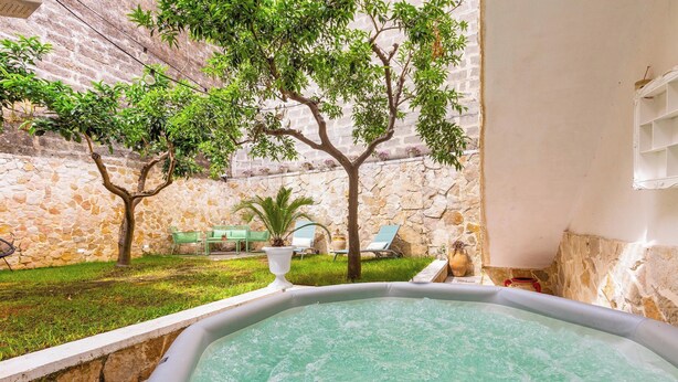 Un bain à remous dans une cour intérieure, avec des murs en pierre, un palmier et des chaises longues.