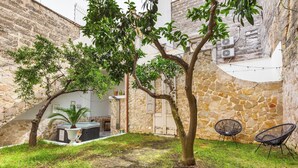 Une cour intérieure avec un mur en pierre, un arbre, un jacuzzi et deux chaises.