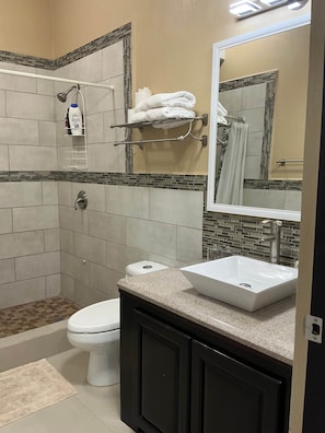 A bathroom with a shower, toilet, two sinks, and a mirror. - Garden City Suite | Modern 2BR Apartment (Belmopan)