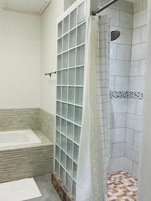 A bathroom with a glass shower enclosure, a bathtub, and tiled walls. - Garden City Suite | Modern 2BR Apartment (Belmopan)