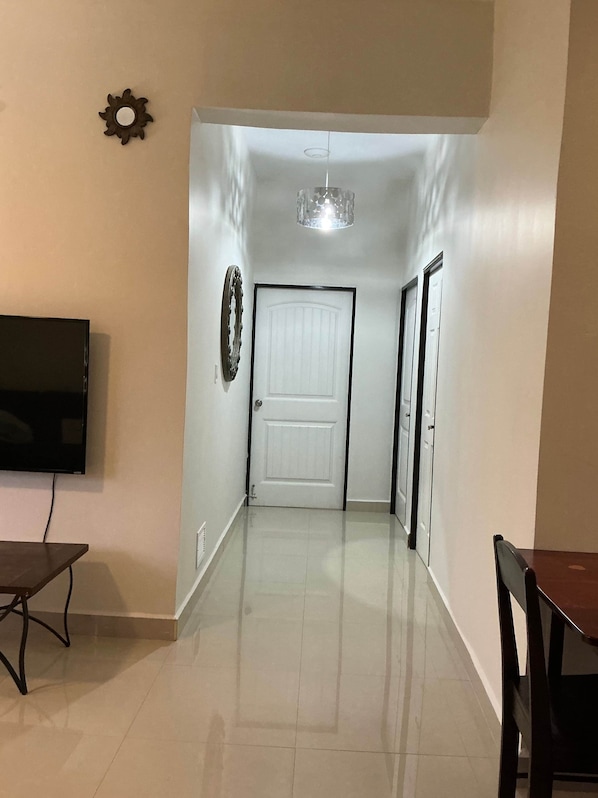 Un pasillo con una puerta blanca, un televisor montado en la pared y un candelabro.