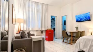 Moderni hotellihuone, jossa on sohva, pieni pöytä, punainen jääkaappi, televisio ja sänky.