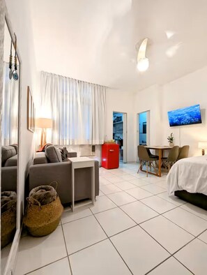 Ein modernes Hotelzimmer mit einer Couch, einem kleinen Tisch, einem roten Kühlschrank, einem Fernseher und einem Bett.