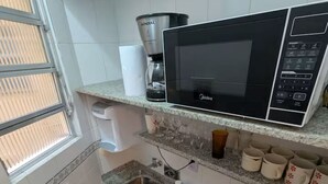 Kompakti keittiö, jossa on mikroaaltouuni, kahvinkeitin ja pieni pesuallas.
