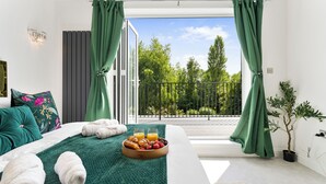 Een slaapkamer met een bed, groene gordijnen, een balkon en een ontbijtarrangement.