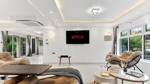 Een moderne woonkamer met een flatscreen televisie, leren banken, een salontafel en uitzicht op groen.