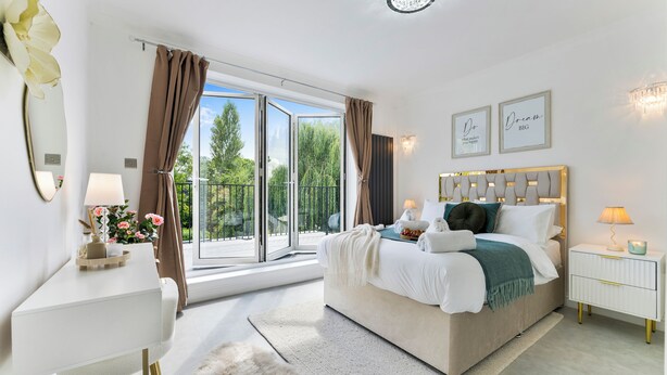Een slaapkamer met een bed, nachtkastjes, een bureau, een groot raam en uitzicht op groen.
