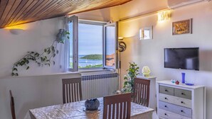 Une pièce comprenant une table, des chaises, un téléviseur et une fenêtre donnant sur la mer.