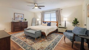 A bedroom with a bed, a desk, a chair, a dresser, a ceiling fan, and a window with curtains. - Pool Home w/ King Beds, 4 TVs & Large Backyard (Valdosta)
