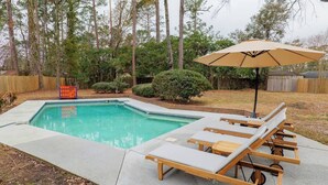 A backyard with a swimming pool, lounge chairs, and an umbrella. - Pool Home w/ King Beds, 4 TVs & Large Backyard (Valdosta)