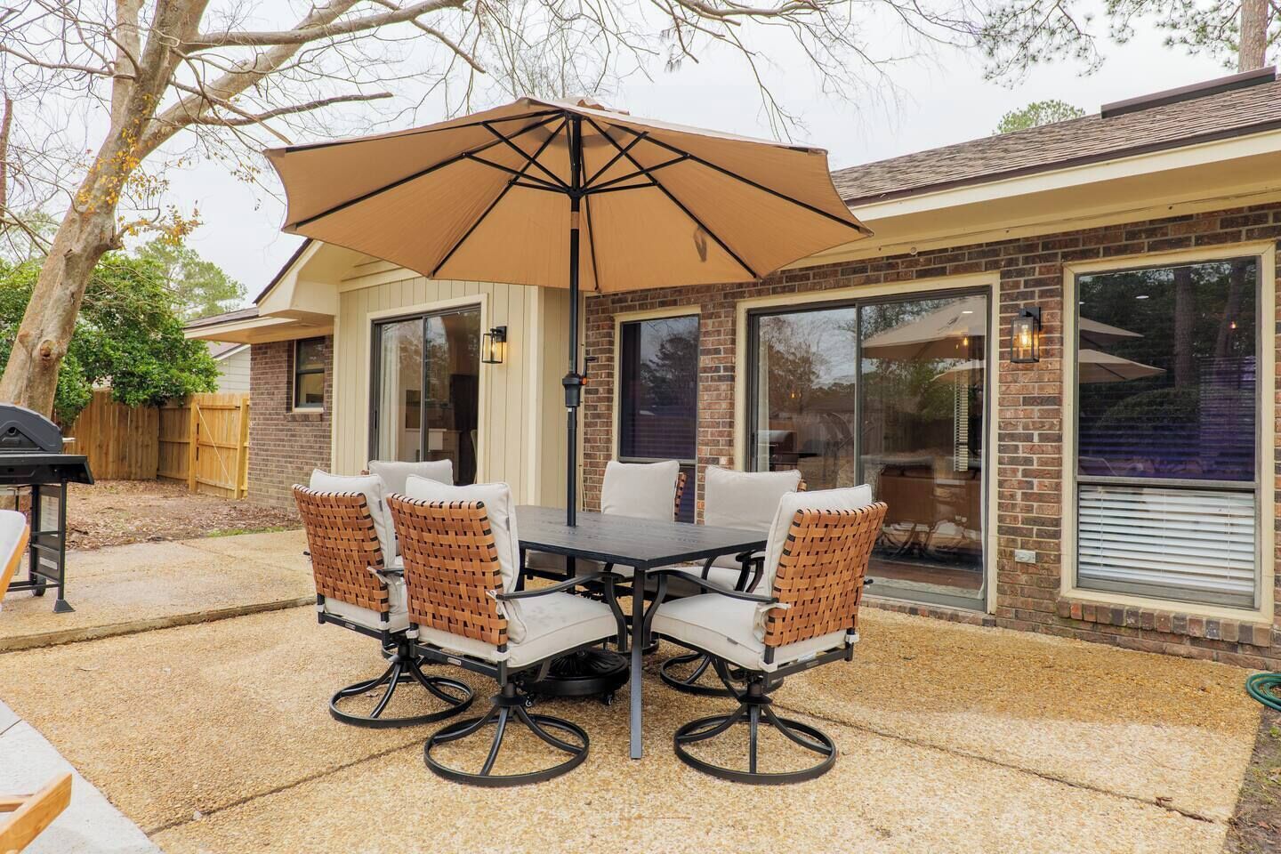 A patio with a table and chairs, an umbrella, and a brick house with large windows.