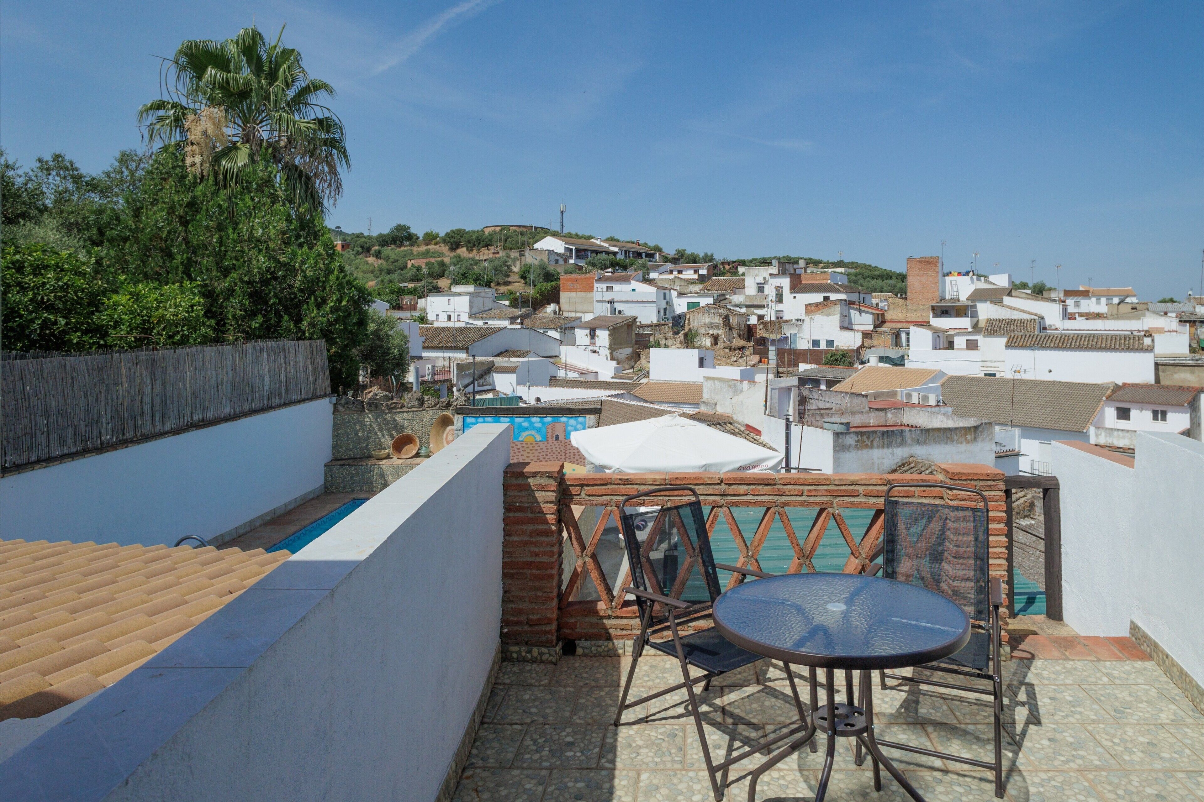 Terraza en la azotea con una mesa y sillas, con vistas a una zona residencial con casas y vegetación.