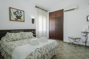 Quarto com cama, guarda-roupa, ar condicionado e uma pequena mesa com uma cadeira.