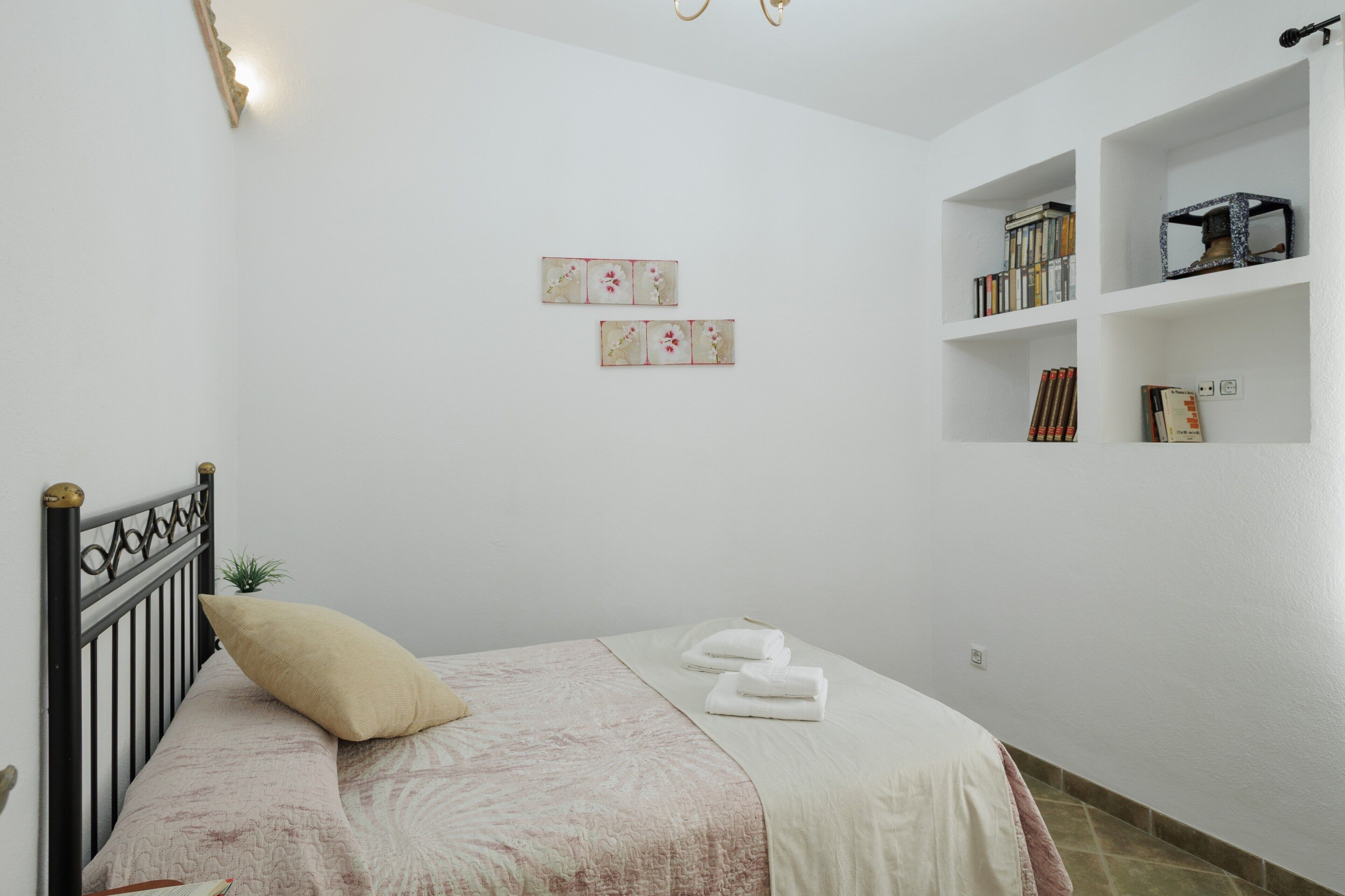 A bedroom with a bed, pillows, a small plant, a bookshelf, and wall art.