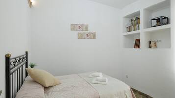 A bedroom with a bed, pillows, a small plant, a bookshelf, and wall art.