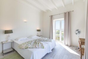 Ein Schlafzimmer mit zwei Betten, einem Nachttisch mit Lampe, einem Fenster mit Vorhängen und einem Ventilator.
