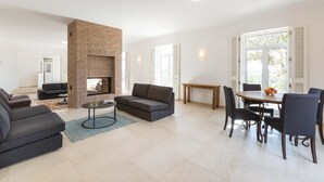 Uma sala de estar moderna com lareira de tijolos, um sofá, uma mesa de centro e um espaço de jantar com mesa e cadeiras.