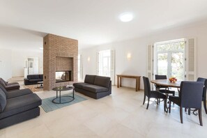 Ein modernes Wohnzimmer mit Kamin aus Backstein, einer Couch, einem Couchtisch und einem Essbereich mit Tisch und Stühlen.
