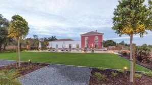 Um edifício grande com fachada vermelha, um gramado bem cuidado e área de piscina com espreguiçadeiras.