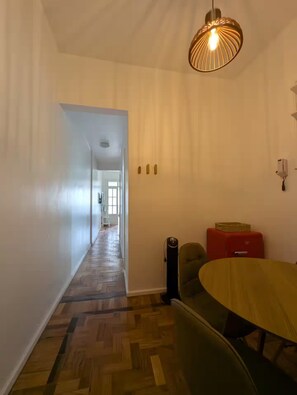 A hallway with a wooden floor, a dining area with a round table and chairs, and a hanging light fixture. - Spacious flat in Copacabana (Rio de Janeiro)
