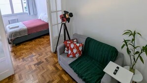 Ein Zimmer mit einem Bett, einem Sofa, einem Deckenventilator, einem Stativ und einer Topfpflanze.