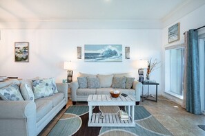 A living room with a sofa, a coffee table, and a painting of a wave on the wall. - Beachfront Townhouse(10) Pet Friendly Covered Deck (Panama City Beach)
