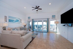 A living room with a beige sofa, ceiling fan, and a view to a balcony. - Beachfront Townhouse(10) Pet Friendly Covered Deck (Panama City Beach)