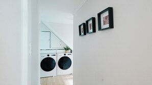 Une buanderie équipée de deux machines à laver, avec une plante en pot et des tableaux encadrés accrochés au mur.
