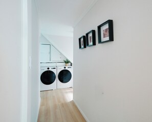 Ein Waschraum mit zwei Waschmaschinen, einem Blumentopf und gerahmten Bildern an der Wand.