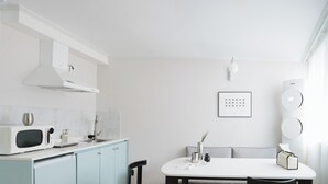 Une cuisine moderne avec un micro-ondes blanc, un évier et un meuble blanc. On y trouve une table à manger avec des chaises et un canapé bleu clair.
