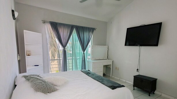 A bedroom with a bed, a ceiling fan, a TV, and a window with curtains. - Arroyito: Small Apartment (Puerto Vallarta)