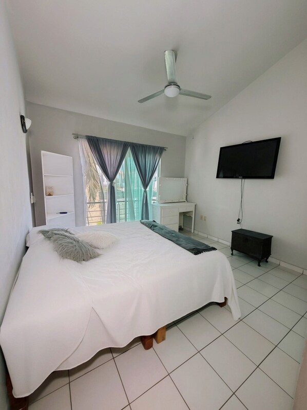 A bedroom with a bed, a ceiling fan, a TV, and a window with curtains. - Arroyito: Small Apartment (Puerto Vallarta)