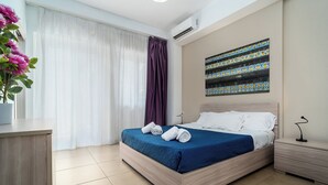 Ein Hotelzimmer mit Bett, Nachttisch, Schreibtisch, einer Zimmerpflanze und einem Fenster mit Vorhängen.