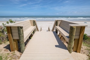 Ein hölzerner Steg führt zu einem Strand mit freiem Blick auf das Meer.