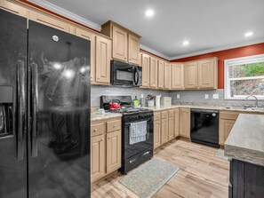 A kitchen with wooden cabinets, a black refrigerator, a microwave, a stove, and a dishwasher. - Peaceful Mountain Retreat | Wraparound Deck (Black Mountain)