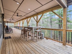 Eine überdachte Terrasse mit Holzwerteln, einem Tisch, Stühlen und einem Schaukelstuhl.
