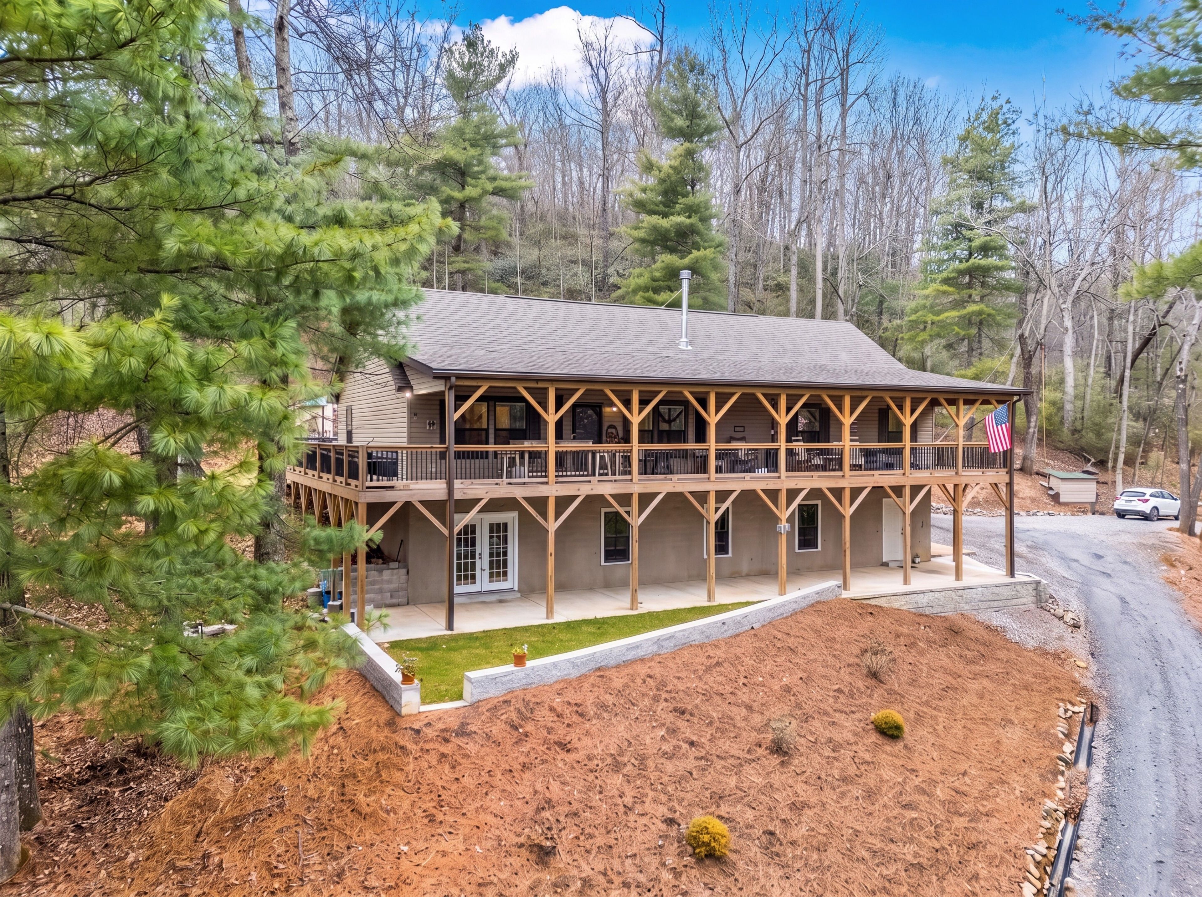 A two-story wooden cabin with a balcony, surrounded by trees and a clear sky.