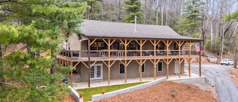 A two-story wooden cabin with a balcony, surrounded by trees and a clear sky.